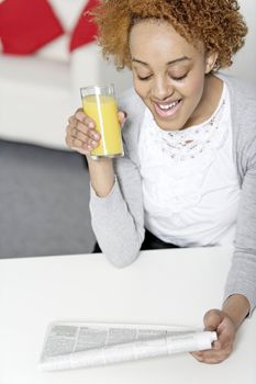 Beautiful young black woman reading a newspaper while enjoying fresh juice