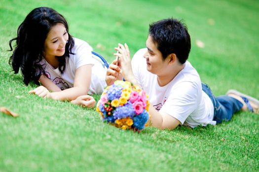 young boy taking her girlfriend photo with his mobile phone on grass