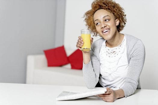 Beautiful young black woman reading a newspaper while enjoying fresh juice