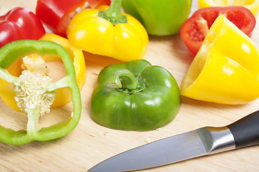 Selection of red green and yellow peppers sliced up on a chopping board