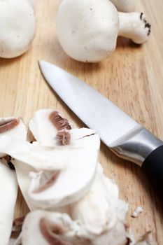 Fresh organic mushrooms being sliced on a wooden chopping board