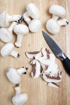 Fresh organic mushrooms being sliced on a wooden chopping board