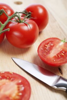 Fresh tomatoes being sliced on a wooden chopping board with knife