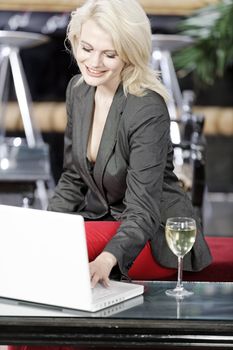 Beautiful young woman chatting with friends on her laptop while enjoying a glass of wine in a bar