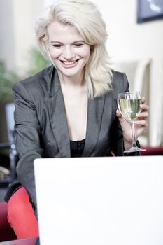 Beautiful young woman chatting with friends on her laptop while enjoying a glass of wine in a bar