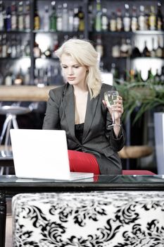 Beautiful young woman chatting with friends on her laptop while enjoying a glass of wine in a bar