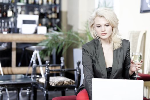 Beautiful young woman chatting with friends on her laptop while enjoying a glass of wine in a bar