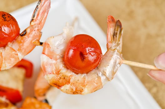 Closeup of grilled shrimps and tomatoes on bamboo sticks with salmon