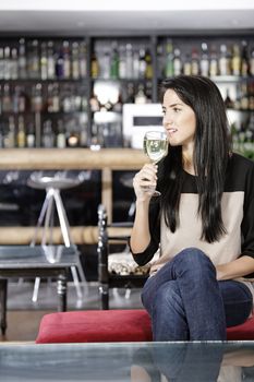 Attractive young woman enjoying a glass of white wine in a wine bar.