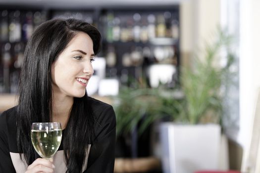 Attractive young woman enjoying a glass of white wine in a wine bar.