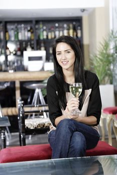 Attractive young woman enjoying a glass of white wine in a wine bar.