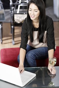 Beautiful young woman chatting with friends on her laptop while enjoying a glass of wine in a bar