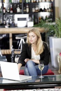 Beautiful young woman chatting with friends on her laptop while enjoying a glass of wine in a bar