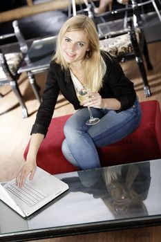 Beautiful young woman chatting with friends on her laptop while enjoying a glass of wine in a bar