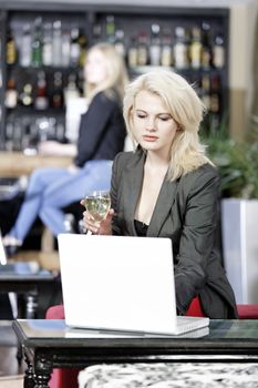 Beautiful young woman chatting with friends on her laptop while enjoying a glass of wine in a bar