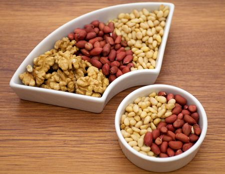 White plats with walnuts, peanut and pine nut isolated on wooden background