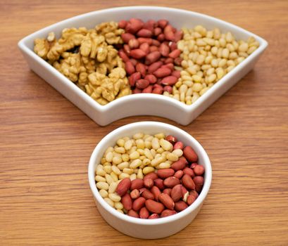 White plats with walnuts, peanut and pine nut isolated on wooden background