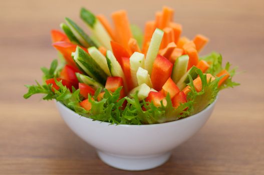 Red Bell pepper, cucumber and carrots straws with salad leaves isolated on wooden background