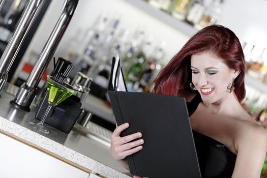 Attractive young woman reading from a wine list at the bar.