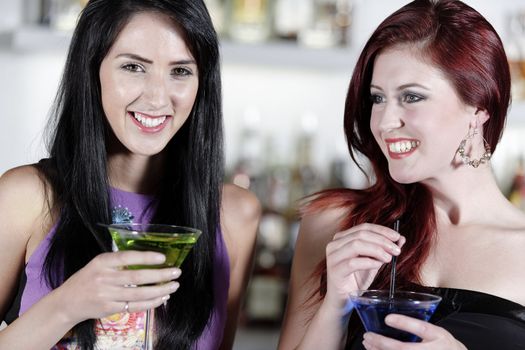 Two beautiful young woman chatting and drinking cocktails at a nightclub or wine bar.