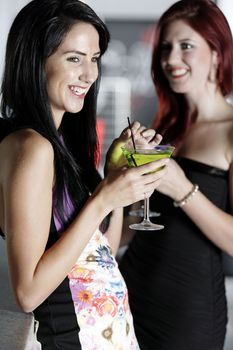 Two beautiful young woman chatting and drinking cocktails at a nightclub or wine bar.