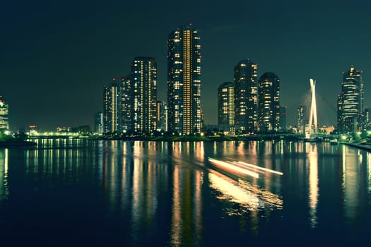 modern Tokyo buildings with night reflection in water and light traces of moving ship, Japan