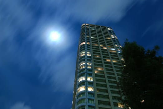 high-rise residential building with fool moon scattering in moving clouds at windy night in Tokyo city, Japan
