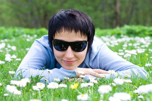 Young woman in sunglasses is lying on the flowering meadow