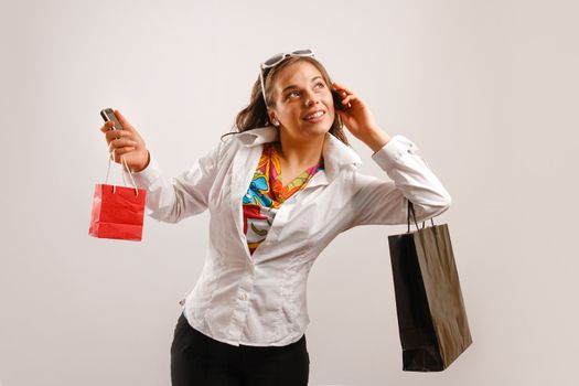 Modern looking young woman wearing white jacket talking on the phone and holding shopping bags