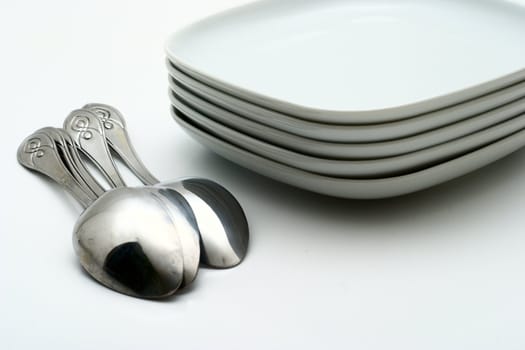 Pile of white plates and shining spoons on a white background. Preparation for table layout.