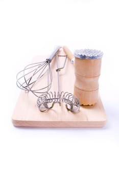 Kitchen utensil set. Meat tenderizer with egg whisks lying on kitchen board. Isolated on white.