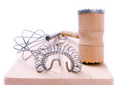 Kitchen utensil set. Meat tenderizer with egg whisks lying on kitchen board. Isolated on white.