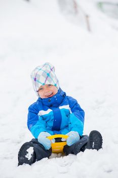 Cute little boy in blue riding on a sled near  the Austrian cottage