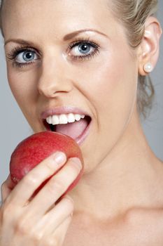 Beautiful young woman eating an apple wearing a white vest top