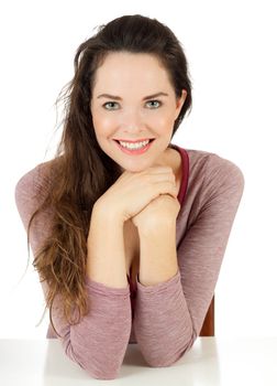 A happy beautiful young woman sitting at a table smiling and looking at camera. Isolated on white.