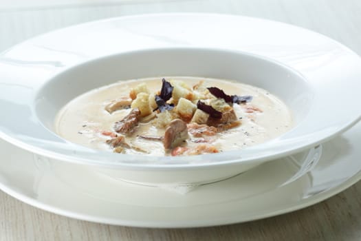 Hot soup in the white dish on wooden table