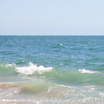 Abstract of a calm blue-green ocean with small breaking wave on the left,