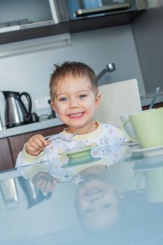Happy little cute boy in pajamas eating breakfast at a table in the kitchen. Vertical view