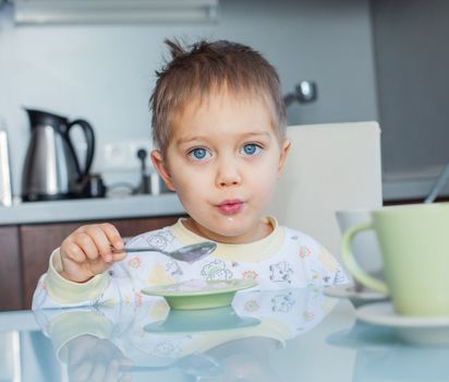 Happy little cute boy in pajamas eating breakfast at a table in the kitchen