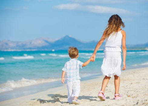 Back view of young beautiful girl and her brather walking at pretty beach. Majorca, Spaine