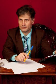 Portrait of middle-aged man working in his home at his desk on a background of red wallpaper