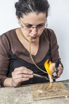 Portrait of a female jeweler working with a flame on a piece of silver wire.
