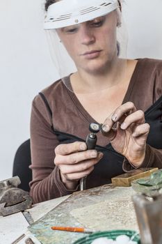Female jeweler polshing a piece of metal in her workshop.