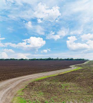 rural road in black agricultural field under cloudy sky