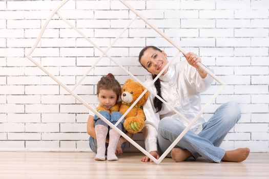 Mother and 5 year old daughter sitting by the wall, holding a frame