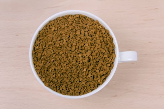 Coffee granules in a white cup on wooden background.