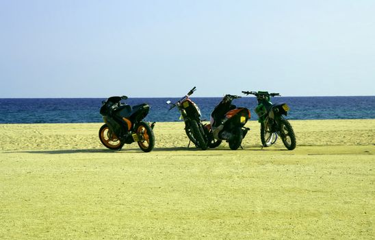 Four motorbikes parking on a beach. Sea in background.