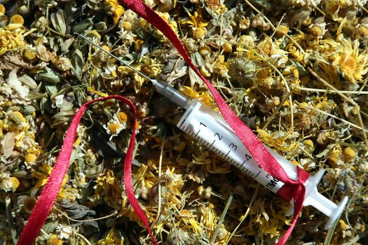 The syringe wound with a red ribbon lies on the dried up flowerses