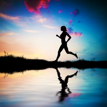 Silhouette of a fit woman running at sunset. Water reflection