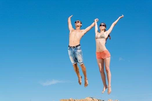 young couple jumping together on a blue sky background